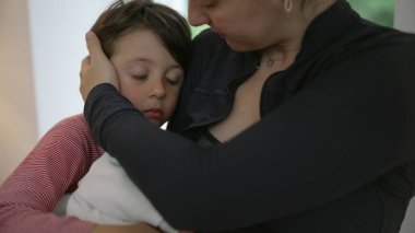 Bir anne kucağında yeni doğmuş bir bebeği kollarında tutarken küçük oğlunu teselli eder. Şefkat ve sevgi dolu bir anı paylaşır. Günlük kıyafetler giyer, duygusal bağ kurar, ebeveynlik yapar, aile desteğini paylaşır.