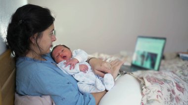 Yeni anne, yeni doğmuş bebeğiyle rahat bir yatakta dizüstü bilgisayarla çalışırken bağ kuruyor. Profesyonel ve ebeveyn sorumlulukları ve modern ebeveynlik arasındaki dengeyi vurguluyor.