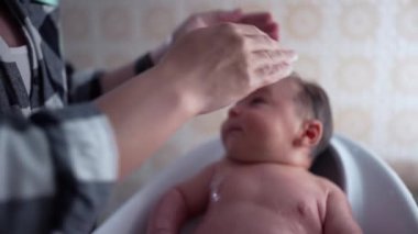 Banyo sırasında başını nazikçe yıkayan bebek, yukarı odaklanan gözler, şefkatli ve şefkatli bir an bakıcıdan gelen şefkatli dokunuşu ve sevgiyi vurgular.