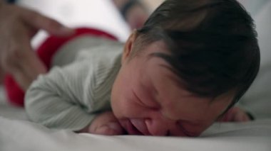 Anne, ağlayan yeni doğmuş bebeğini nazikçe yataktan kaldırıyor. Rahatlatıcı bir dokunuşla sıkıntılı bebeği sakinleştiriyor. Bakım bakımını vurguluyor ve hassas bir anda bağ kuruyor.