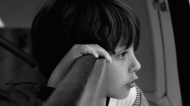 Genç çocuk pencereden dikkatlice dışarı bakıyor, kendi yansımalarında kayboluyor, derin bir düşünce ve iç gözlem sahnesi yaratıyor, siyah ve beyaz.