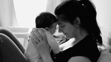 Anne ve bebek sevgi dolu alın dokunuşlarını paylaşıyor, derin duygusal bağları ve sevgiyi sembolize ediyor, hem sakin, hem samimi, hem de sessiz, siyah ve beyaz bir şekilde gülümsüyor.