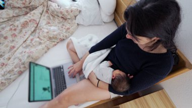 Anne yeni doğmuş bir bebeği kucağında tutarken dizüstü bilgisayarla birden fazla iş yapıyor, uzaktan çalışma ve ebeveynliği dengeliyor, modern çalışan annelerin zorluklarını ve adanmışlığını vurguluyor