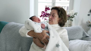 Yaşlı bir kadın sevgiyle yeni doğmuş bebeği bir battaniyeye sardı, hassas aile bağları, büyükannenin bakımı, huzurlu ev ortamı, nesiller arası bağ.