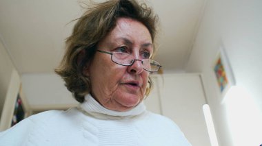 Gözlüklü yaşlı bir kadın düşünceli bir ifadeye sahiptir, derin düşüncelere dalmış. Düşünceli duygu ve içsel ruh hali bilgeliği ve yansıtıcı anları vurguluyor.