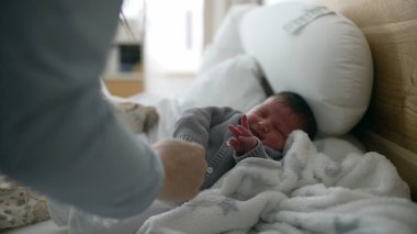 Anne ağlayan bebeği yataktan kaldırıyor, yumuşak battaniyeye sarılıyor, hassas bakım ve rahatlık anı, duygusal bağ, erken annelik.