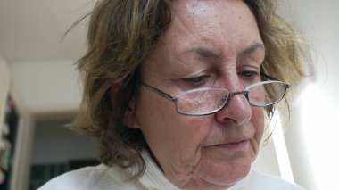 Okumaya dalmış, gözlük takan yaşlı bir kadının yakın çekimi. edebiyatın ve hayat boyu öğrenmenin zevkini vurgulayan sakin atmosfer ve odaklanmış ifade.