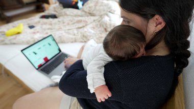 Anne kucağında yeni doğmuş bir bebek varken dizüstü bilgisayarda çalışıyor, mesleki görevlerin ve ebeveynlik sorumluluklarının dengesini gösteriyor, modern aile yaşamını ve çoklu görev becerilerini vurguluyor