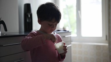 Genç çocuk modern bir mutfakta atıştırmalık yiyor, doğal ışık sahneyi aydınlatıyor, çocukluğun basit, günlük bir anını yakalıyor, gençliğin masumiyetini ve neşesini vurguluyor.
