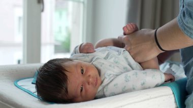 Yeni doğan bebek masanın üzerinde üzerini değiştiriyor, annesinin elinden nazikçe tutuyor. anne ile bebek arasında günlük rutin bir rutin sırasında özel bir bağ olduğunu gösteriyor.