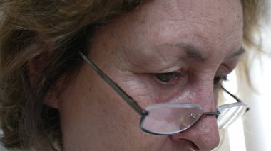 Düşünceli, düşünceli, gözlüklü, yaşlı bir kadının odaklanmış gözlerinin aşırı yakın çekimi. Konsantrasyon, bilgelik ve içgözlem derinliği, onun iç düşüncelerini vurguluyor.