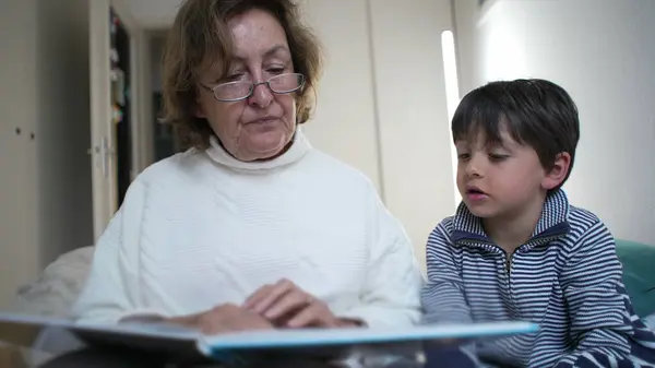 stock image Grandmother pointing at a book page while reading to her grandson. educational aspect of storytelling and the close bond between generations through shared reading experiences