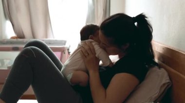 Anne, bebeğiyle şefkatli bir öpücük paylaşıyor. Sevgi ve sıcaklıkla dolu huzurlu, huzurlu bir yatak odasında güçlü bağlarını ve derin sevgilerini vurguluyor.