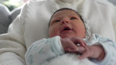 Yenidoğan sakince dinleniyor, sıcaklığa ve güvenliğe sarılmış, merakla bakıyor, huzurlu ve rahatlatıcı bir aile ortamında yeni hayatın masumiyetini ve mucizesini yansıtıyor.