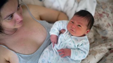 Yeni doğmuş bebek annesinin kollarında dinleniyor, sakin ama meraklı bir ifade sergiliyor. Hayatın ilk anları anne ve çocuk arasındaki derin bağlantıyı ve bakımı vurguluyor.