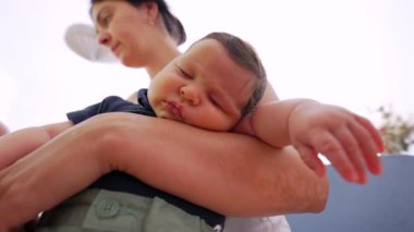 Bebek, annesinin kollarında mışıl mışıl uyuyor. Anne, aydınlık ve havadar bir alanda duruyor. Bu, aile hayatının huzur dolu ortamını yansıtıyor.