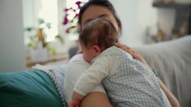 Anne bebeğini bir koltukta otururken kucaklıyor, gözleri bir anlık sükunetle kapanıyor. Sahne anne ve çocuk arasındaki derin bağı ve güven duygusunu yakalıyor.