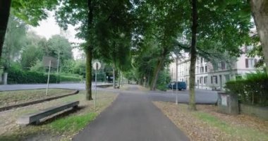 Çevresi yeşillik ve konut binalarıyla çevrili ağaçlarla kaplı kentsel bir yolun manzarası, açık hava yürüyüşleri ve rahatlama için huzurlu ve sakin bir ortam sunuyor.