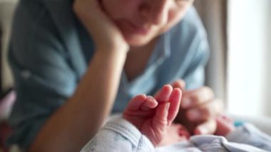 Ebeveynler sevgi dolu bakışlar atarak ebeveynliğin ilk zamanlarını ve derin duygusal bağlarını resmederken yeni doğan bebeğin minik ellerine odaklanmak. Korunma ve bakımı simgeler.