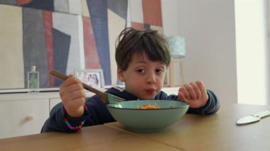 Küçük çocuk yoğun bir şekilde çatalla spagetti çevirmeye odaklanmış, sıcak bir yemek zamanında bir çatışma anını ve çabayı yakalıyor