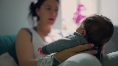 Anne bebeğini kucağında tutuyor. Sıcak, güneşli bir odada etkileşimlerine odaklanıyor. Şefkatli bir an, anne ve çocuk arasındaki bağı yakalıyor.