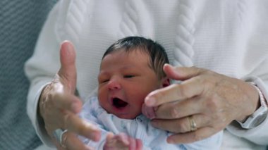 Büyükannem sevgiyle yeni doğan bebeğin elini tutuyor, bir koruma ve bakım jesti, ailenin en yaşlısı ve en küçüğü arasındaki kalıcı bağı ve sıcaklığı simgeliyor.