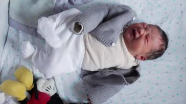 Yenidoğan bebek geriliyor ve ağlıyor, ilk hayatın ham duygularını ve fiziksel ifadelerini yumuşak, rahatlatıcı bir ortamda sergiliyor, hassasiyeti ve hassasiyeti vurguluyor.