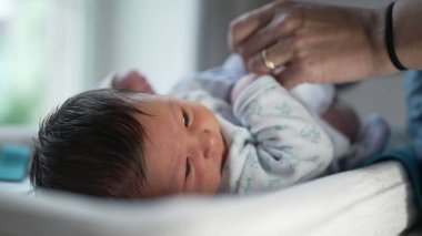 Yeni doğan bebeğin üstünü değişen bir masanın üzerinde yakın plan fotoğrafı, bebeğin bacağını tutan anne, bir evde rutin bebek bezi değiştirme sırasında etkileşimi yakalayıp bağ kuruyor.