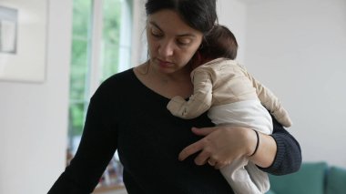 Anne, yeni doğmuş bebeği kucağında tutarken yemek servisi yapıyor, yemek saatinde birden fazla iş yapıyor, ebeveynlik dengesini yakalıyor, sevgi ve özen gösteriyor, özel bir bakım ve günlük yaşam anı yaşıyor.