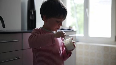 Genç çocuk modern bir mutfakta atıştırmalık yiyor, doğal ışık sahneyi aydınlatıyor, çocukluğun basit, günlük bir anını yakalıyor, gençliğin masumiyetini ve neşesini vurguluyor.