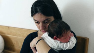 Anne, yeni doğmuş bir bebeği dizüstü bilgisayar kullanırken kucağında tutarak iş ve ebeveynliği dengelemek, modern aile hayatının zorlukları, çoklu görevler ve çalışan ebeveynlerin sorumlulukları