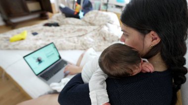 Anne kucağında yeni doğmuş bir bebek varken dizüstü bilgisayarda çalışıyor, mesleki görevlerin ve ebeveynlik sorumluluklarının dengesini gösteriyor, modern aile yaşamını ve çoklu görev becerilerini vurguluyor
