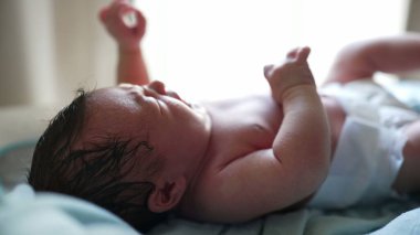 Yeni doğmuş bebek uzanmış, sadece bebek bezi giyiyor, yumuşak ışıkla aydınlatılıyor, hayatın ilk anları, narin cilt ve yüz hatlarını gösteriyor, huzurlu ve huzurlu bir sahne, masumiyeti vurguluyor.