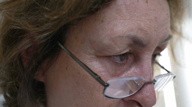 Düşünceli, düşünceli, gözlüklü, yaşlı bir kadının odaklanmış gözlerinin aşırı yakın çekimi. Konsantrasyon, bilgelik ve içgözlem derinliği, onun iç düşüncelerini vurguluyor.