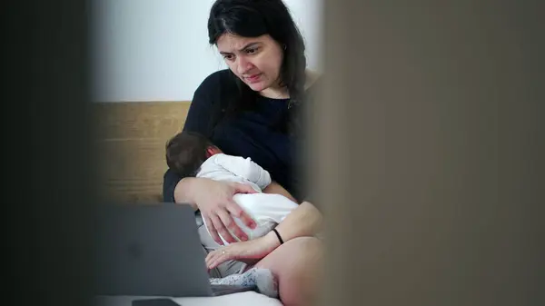 stock image Mother holding newborn baby while working on a laptop, the balance between parenthood and professional life, multitasking, family love, and the modern challenges of working parents