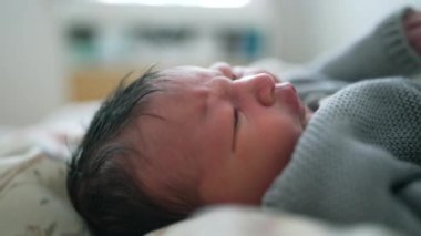 Sıcak bir battaniyeye sarılı yeni doğmuş bebek, kaşlarını çatmış, rahatsızlık belirtileri gösteriyor, erken yaşlardaki duygusal anlar, bebek ifadesi ve sıcak ortam.