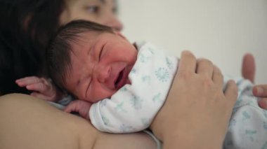 Annenin ağlayan bir bebeği kucağına alıp bebeğe güven ve sevgi sağlayan duygusal bağlantıya ve rahatlatıcı kucaklamaya odaklandığı yakın plan.