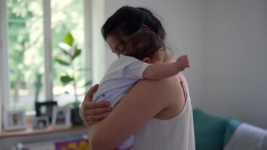 Anne, bebeğini gözleri kapalı kucaklıyor. Yumuşak ve huzurlu bir anın tadını çıkarıyor. Kapalı bir ortamda sevgi ve bağlılık.