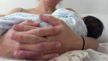 Annenin, yeni doğan bebeğini emzirme seansında kucakladığı yakın çekim. Görüntü, anneliğin ilk aşamalarında paylaşılan koruyucu ve besleyici bağı vurgular.