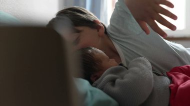 Büyük kardeş ve bebek bir yatakta sevgi dolu, güneşli, oyuncaklarla dolu sıcak bir odada hassas ve neşeli anlar paylaşıyorlar, güçlü bir kardeş bağı ve neşeli bir aile ortamı sergiliyorlar.