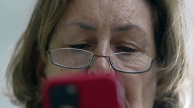 Akıllı telefon kullanan, gözlük takan ve ekrana odaklanan, teknolojiye odaklanan yaşlı bir kadının yüzünü yakından çekerek detaylı ve samimi bir anı yakalıyoruz. 
