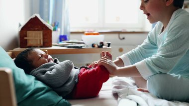 Büyük kardeş bebeğin ayaklarını nazikçe tutuyor. Güneşli bir odada, sıcak bir yatakta oyuncaklarla ve masada zencefilli bir evde. Yürek ısıtan bir bağ ve şefkat anı sergiliyor. 