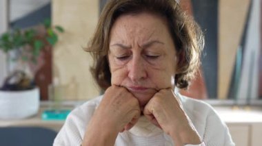 Olgun bir kadın, düşünceli bir anda, çenesini ellerinin üzerinde dinlendiriyor, derin düşüncelere dalmış, deneyimin çizgilerini vurguluyor ve düşünceli ruh halini parlak, kapalı bir ortamda gösteriyor.