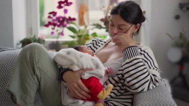 Kollarında bebeğini tutan odaklanmış bir anne, bir koltukta oturup, sıcaklık ve bağ ile dolu huzurlu bir aile sahnesi yaratıyor..