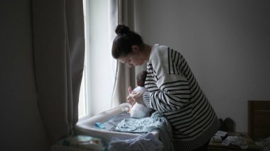 Anne sevgiyle yeni doğmuş bebeğini pencerenin yakınındaki bir masanın üzerine koyar, sıcak bir evde huzurlu ve şefkatli bir anı yakalar.