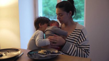 Anne yeni bebeğini kucağında tutarken, büyük kardeş sevgiyle bebekle etkileşime giriyor. Yemek masasındaki iç açıcı sahne aile bağlarının özünü yakalar.