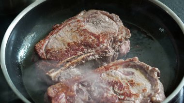 Sıcak tavada pişen biftekler, kahverengileşmeye başlıyor, taze sığır eti, cızırtılı ses, ev mutfağı, mutfak hazırlığı, lezzetli bir yemek hazırlama, pişirme sürecinin detaylı görüntüsü.