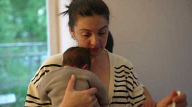 Anne, büyük çocuğunu azarlarken yeni doğmuş bebeğini bir inançsızlık ifadesiyle kucaklıyor. Aile ilişkilerinin dinamiği ve annenin özenli doğası.