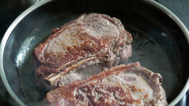 Sıcak tavada pişen biftekler, kahverengileşmeye başlıyor, taze sığır eti, cızırtılı ses, ev mutfağı, mutfak hazırlığı, lezzetli bir yemek hazırlama, pişirme sürecinin detaylı görüntüsü.