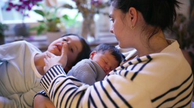 Anne yeni doğan bebeğini nazikçe tutarken, büyük kardeş eğilip, bir aile birlikteliği ve sevgi anı sergiliyor. Sahne, aralarındaki bağları yakalar.